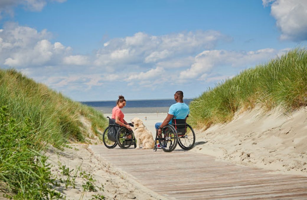 Langeoog: Paar mit Rollstühlen in den Dünen unterwegs