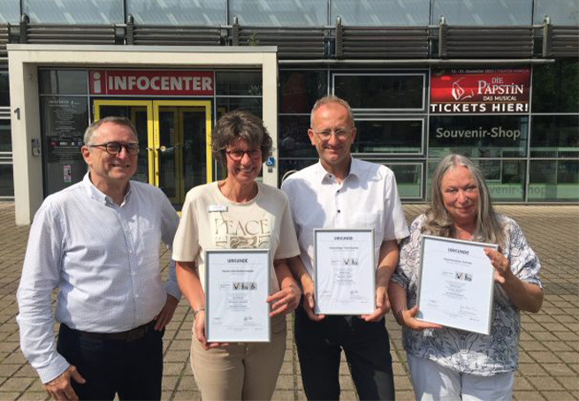 Vor dem Infocenter in Hameln präsentieren von links der HMT-Geschäftsführer Harald Wanger, Mitarbeiterin und Qualitätsbeauftragte Nicole Titz, der Leiter Hallenmanagement Oliver Meinecke und Hallen-Mitarbeiterin sowie Qualitätsbeauftragte Angela Koelman stolz die „Reisen für alle“-Urkunden, die sie für barrierefreie Angebote erhalten haben. © Hameln Marketing