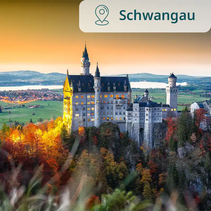 Schloss Neuschwanstein leuchtet im Abendlicht vor herbstlicher Landschaft.