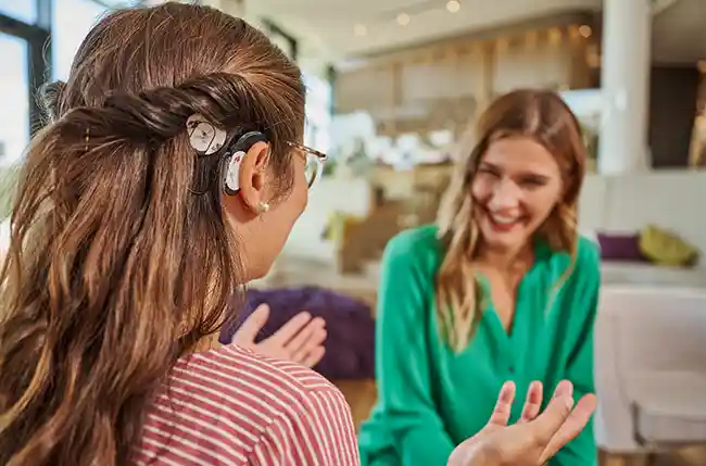 Zwei Frauen sitzen in einem hellen Raum im Seezeitlodge Hotel & Spa in Nohfelden. Eine Frau hat ein Cochlea-Implantat und sie unterhalten sich.