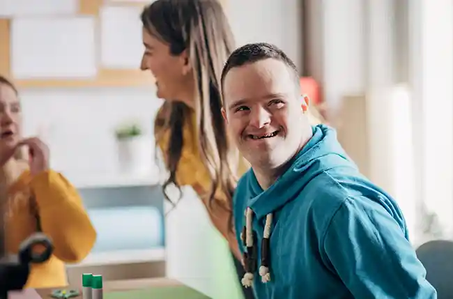 Junger Mann mit Down-Syndrom lächelt in einem Kreativraum.