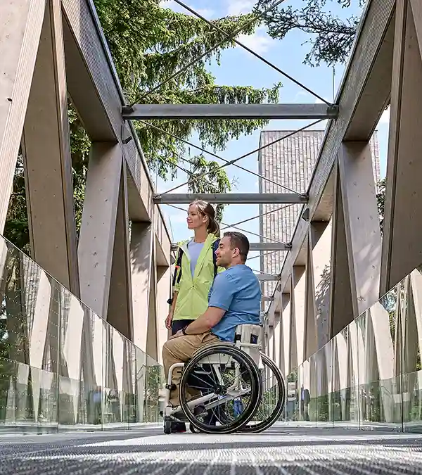 Eine Person im Rollstuhl und ihr Begleiter befinden sich auf einer Brücke in Baiersbronn und blicken auf den Schwarzwald.