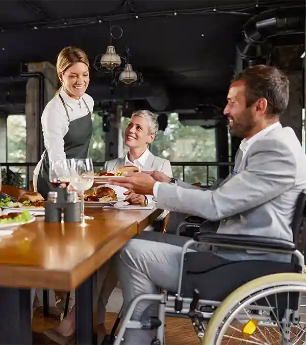 Kellnerin serviert Essen an Mann im Rollstuhl in einem Restaurant.