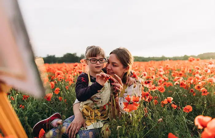 Mutter und Kind mit Down-Syndrom malen zusammen im Mohnblumenfeld.