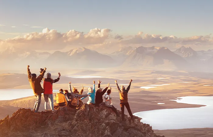 Gruppe feiert gemeinsam den Gipfelblick mit erhobenen Armen auf einem Berg bei Sonnenuntergang.