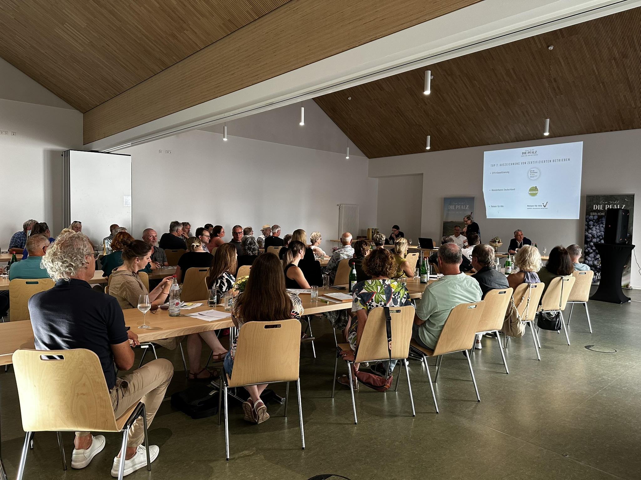 Viele Personen sitzen auf Stühlen in einem Raum. Es handelt sich im eine Mitgliederversammlung.